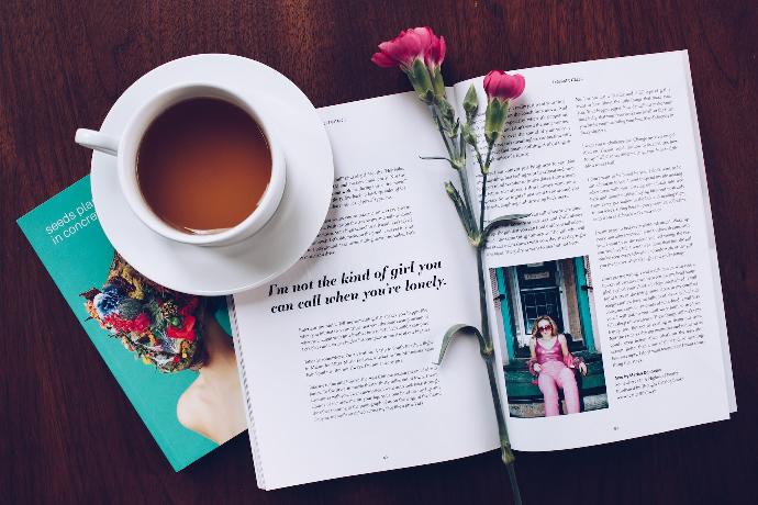 opened book with pink flower on top near filled ceramic mug